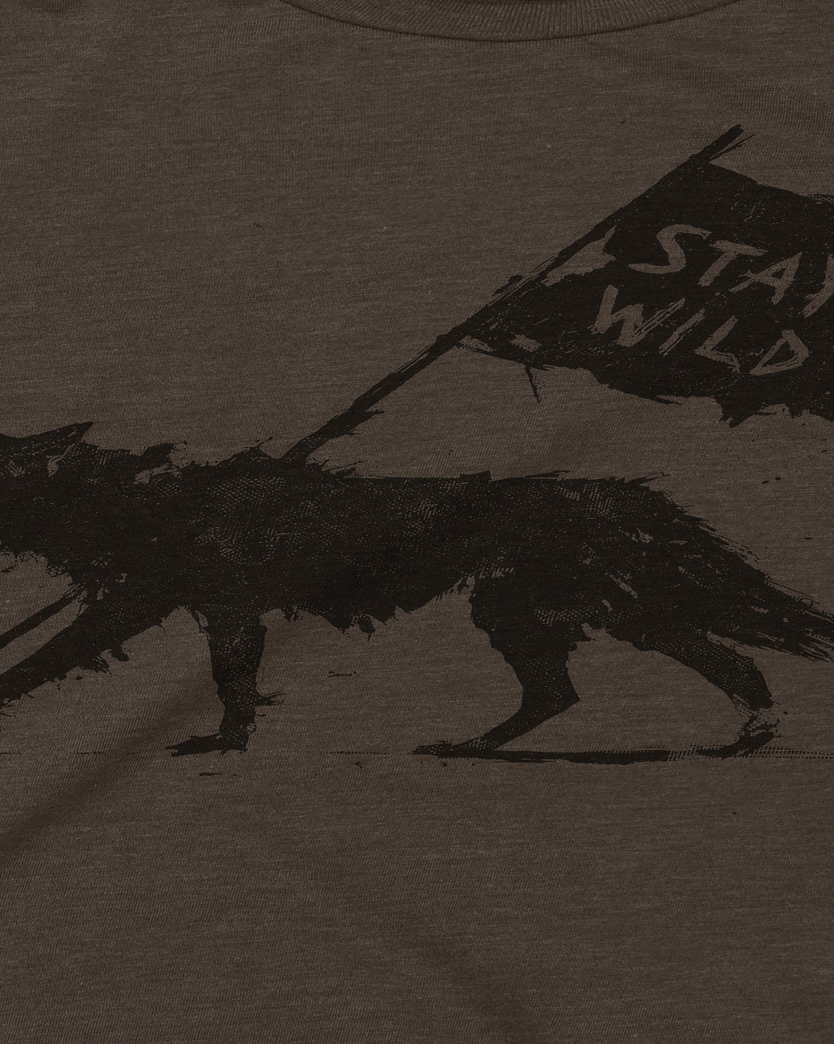 Close-up of a dark heather brown t-shirt featuring a distressed black graphic of a wolf carrying a flag that reads 'STAY WILD'.