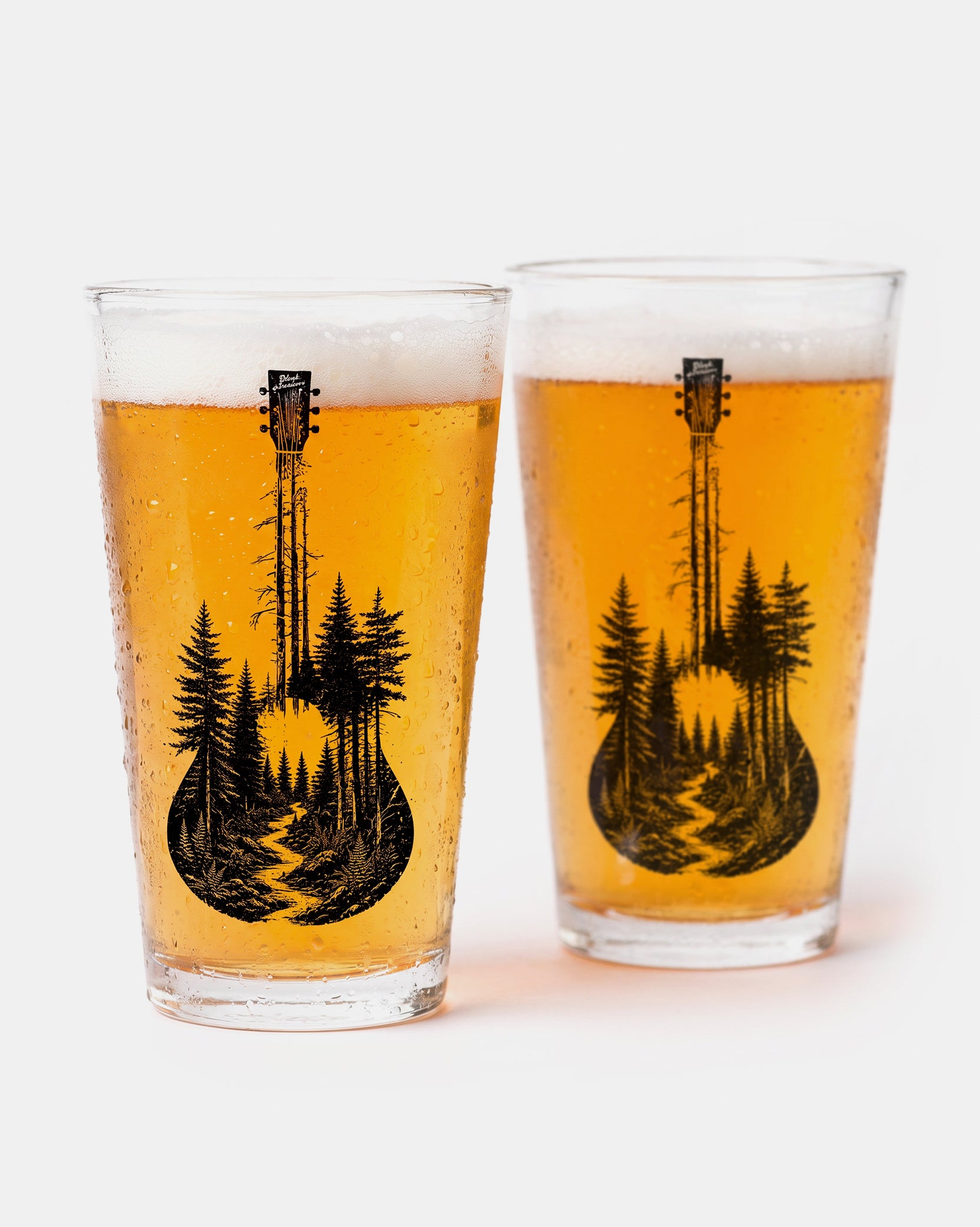 Two clear drinking glasses filled with golden beer and foam, each printed with a black silhouette of a guitar shaped like a pine forest, on a clean white background.