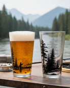 Two glasses with tree and fishing design on a wooden surface with a scenic background