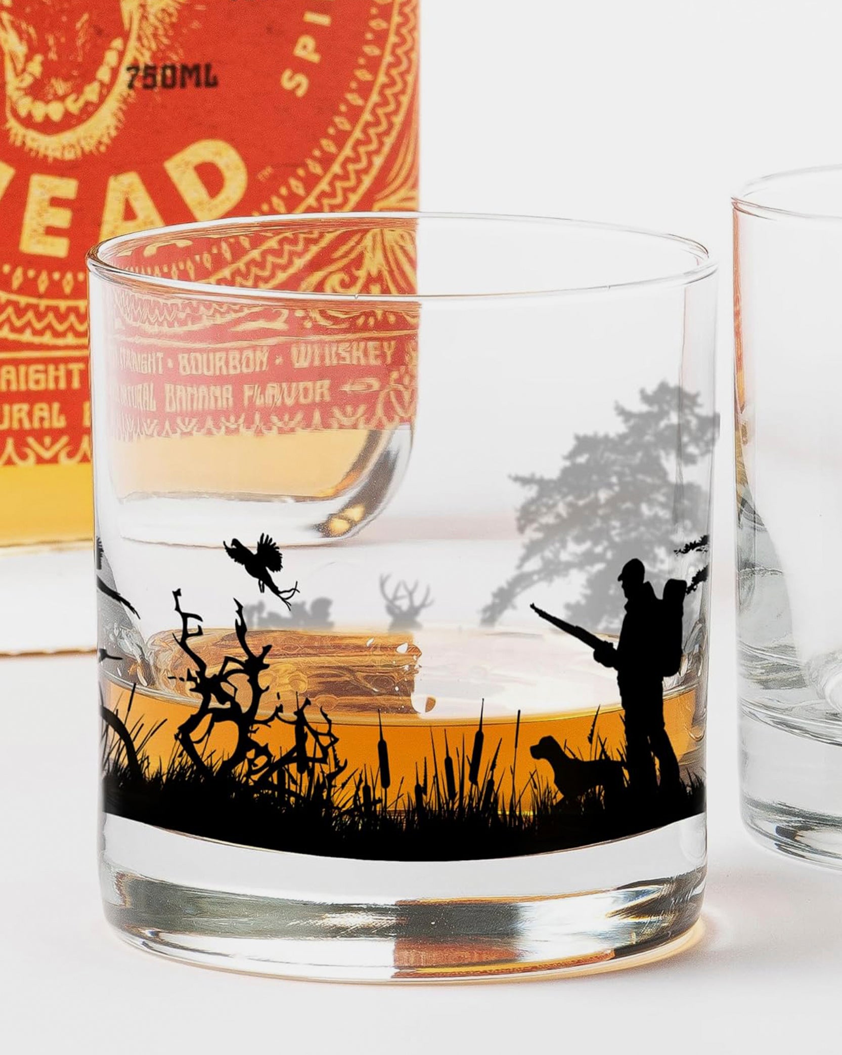 Glass with hunting scene engraving next to a bottle of whiskey